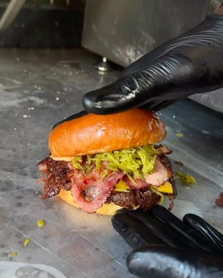 Smashburger mit Bacon, Cheddar und Pickles wird auf der Grillplatte zusammengesetzt