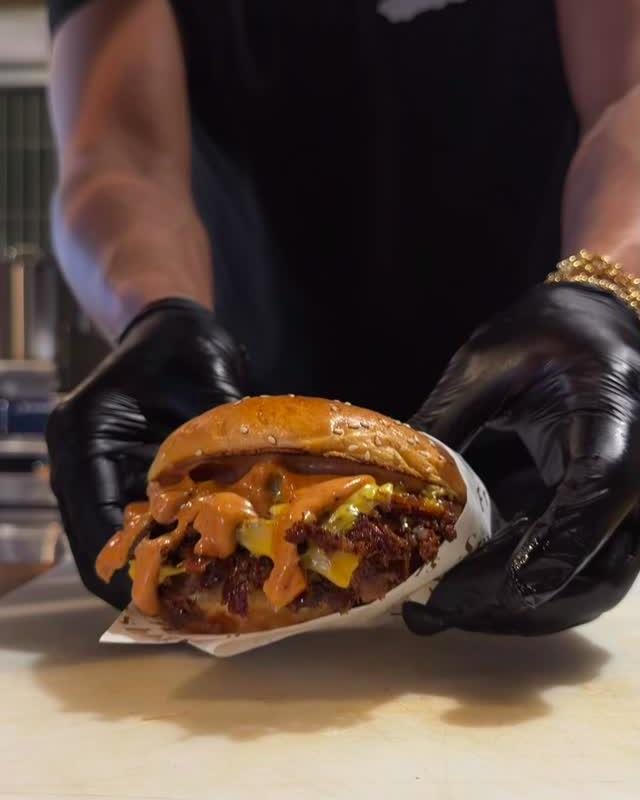 Smashburger mit oranger Fro Sauce, in schwarzen Handschuhen präsentiert