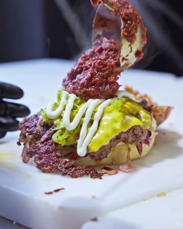 Burger mit Suya-Topping, Käse, Pickles und weisser Sauce