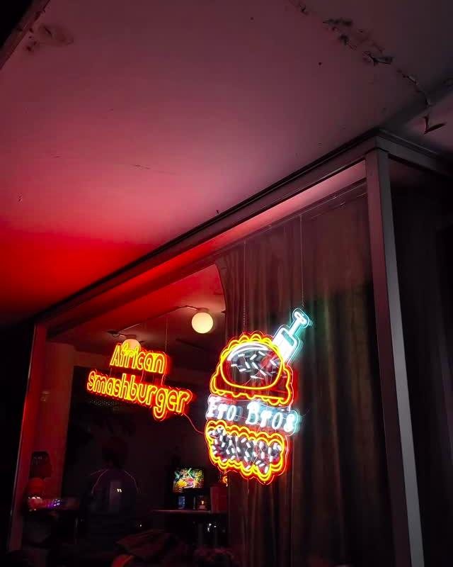 Neon-Schilder «African Smashburger» und «Fro Bros» im Schaufenster bei Nacht